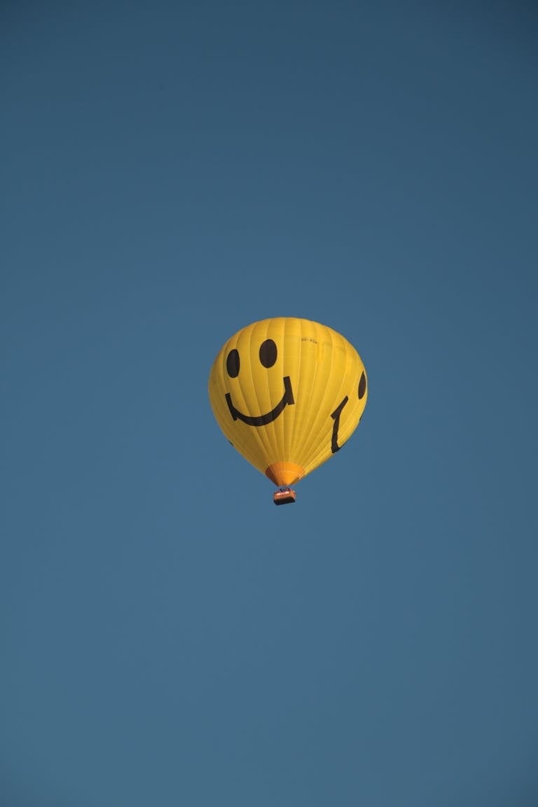 A vibrant yellow smiley balloon floats against a clear blue sky, symbolizing joy and freedom.