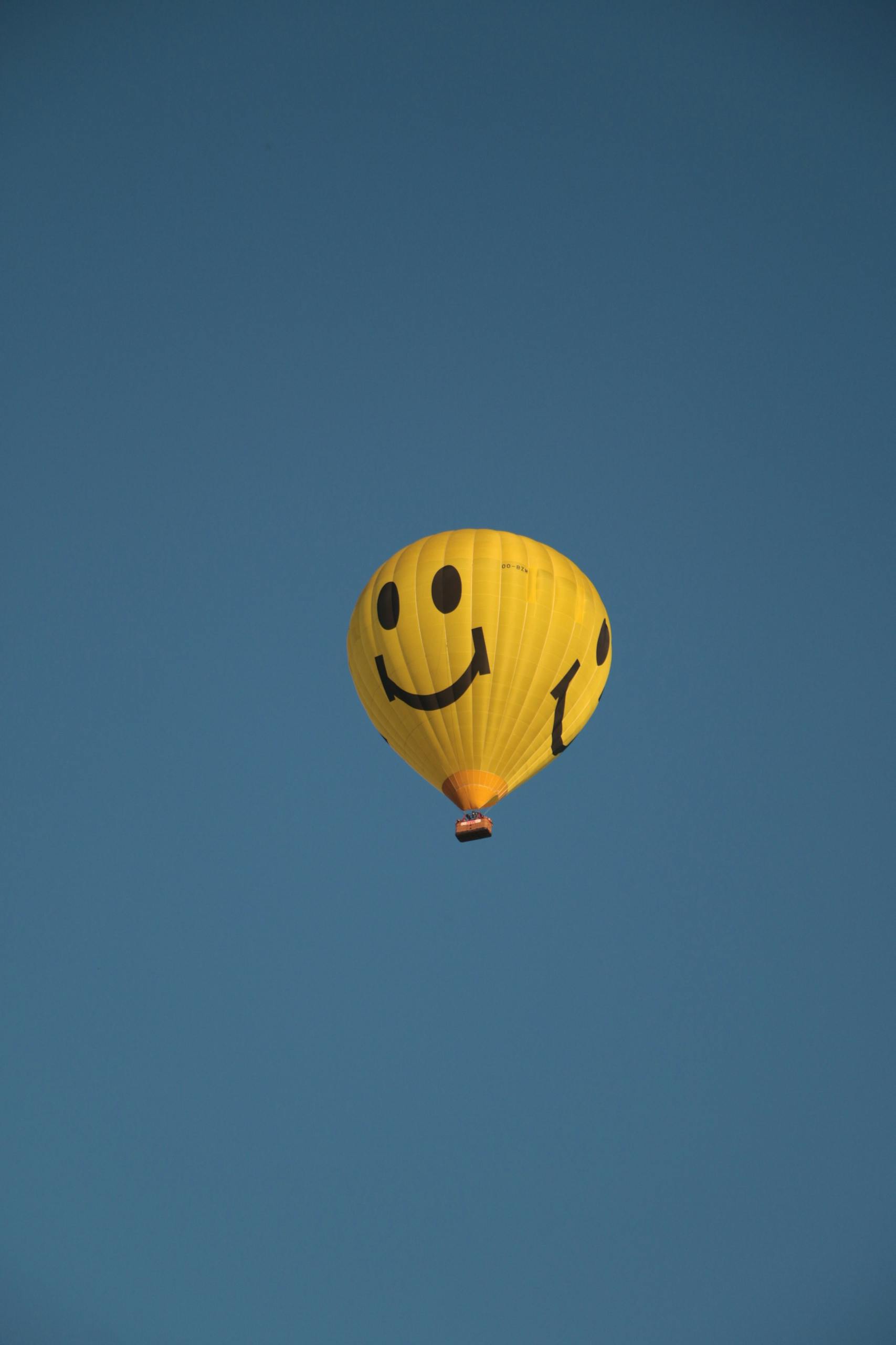 A vibrant yellow smiley balloon floats against a clear blue sky, symbolizing joy and freedom.